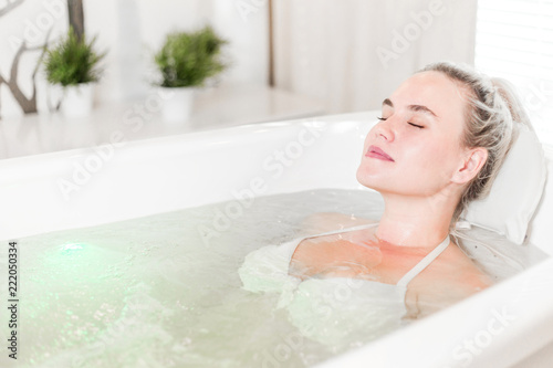 Relaxed girl with closed eyes lying in a white Jacuzzi in a beauty salon caring for her body