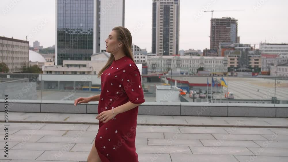 Attractive girl in a red dress goes down the street in a city Attractive girl in a red dress goes down the street in a city
