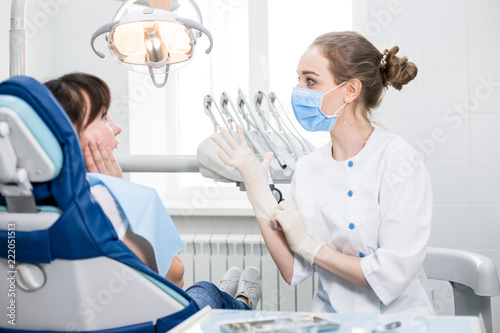 Fototapeta Naklejka Na Ścianę i Meble -  Beautiful girl dentist in white uniform wears latex gloves preparing for dental treatment in patients