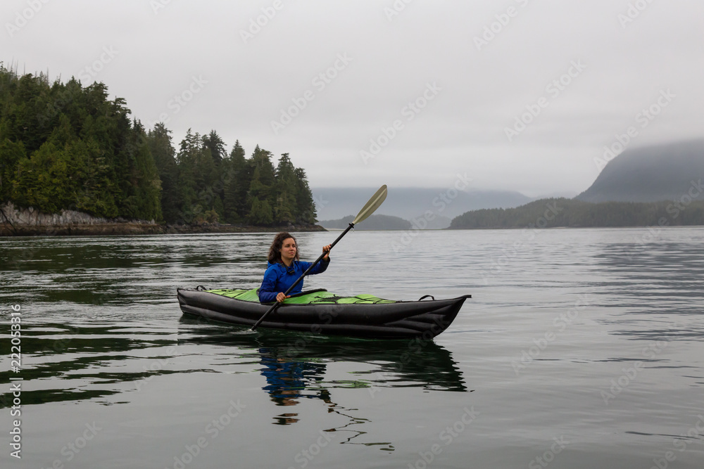 Girl kayaking in the ocean during a cloudy and gloomy sunrise. Taken in Tofino, Vancouver Island, BC, Canada.