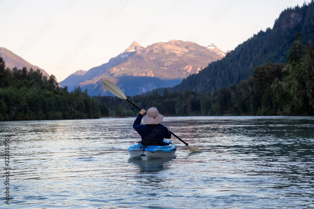 Kayaking in a river surrounded by Canadian Mountains during a vibrant summer sunset. Taken in Squamish, British Columbia, Canada.