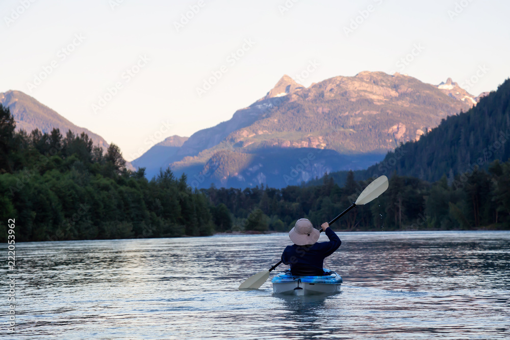 Kayaking in a river surrounded by Canadian Mountains during a vibrant summer sunset. Taken in Squamish, British Columbia, Canada.
