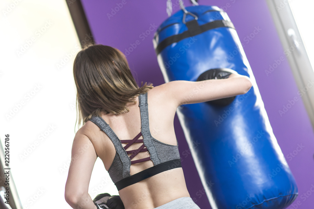 Young woman training to become a boxer, punching a bag in a gym