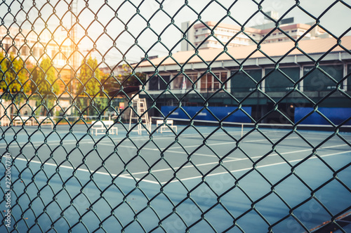 Metal mesh wire fence with tennis court in blurry for background.