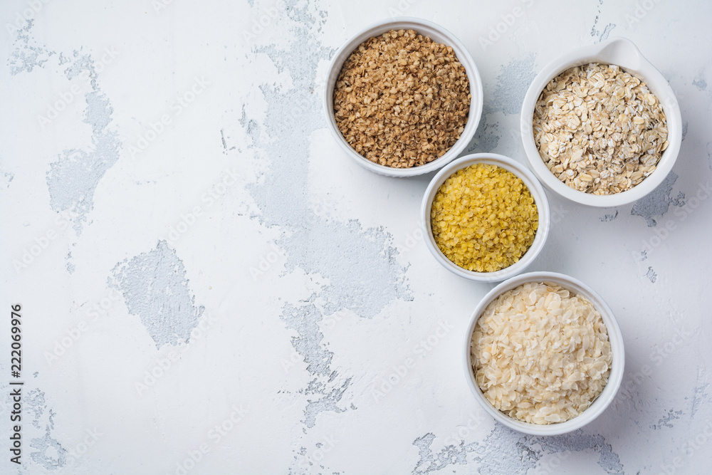 Variety of cereal flakes rice, millet, buckwheat, oatmeal. Superfood in white ceramic bowls on light wooden background. Top view. Variety of cereal flakes rice, millet, buckwheat, oatmeal. Superfood in white ceramic bowls on light wooden background. Top view.