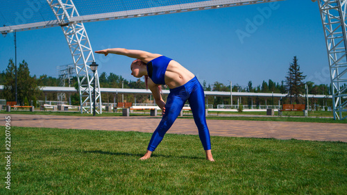 Girl on street workout makes slopes to sides. She is standing barefoot on lawn. Yoga outdoors. Healthy lifestyle.