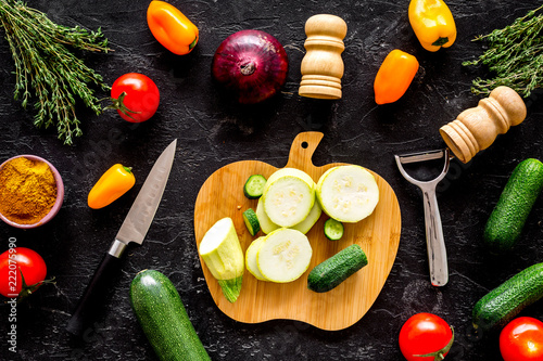 Cooking vegetable stew concept. Fresh vegetables squash, bell pepper, tomato, spices and cutting doard on black background top view photo