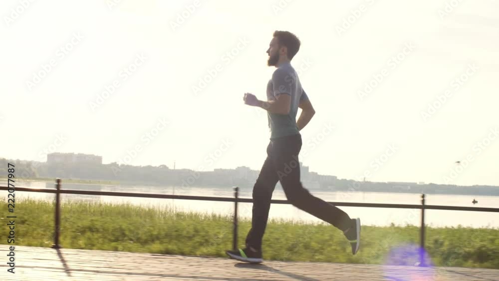 Side view of man running on lakeside promenade at sunrise while working out outdoors in the morning Side view of man running on lakeside promenade at sunrise while working out outdoors in the morning