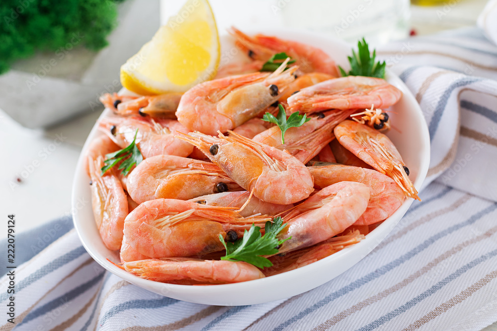 Boiled shrimps or prawns on a white bowl on a white table. Seafood. Boiled shrimps or prawns on a white bowl on a white table. Seafood.