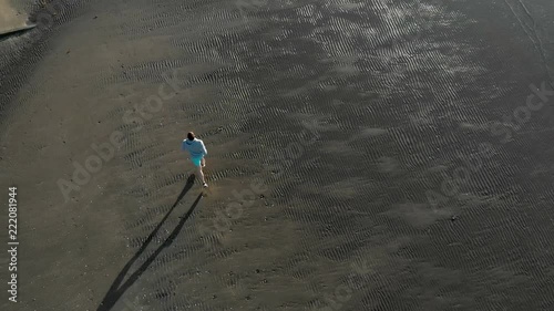 Aerial top down tracking shot of young caucasian man running on a beach in Auckland, New Zealand photo