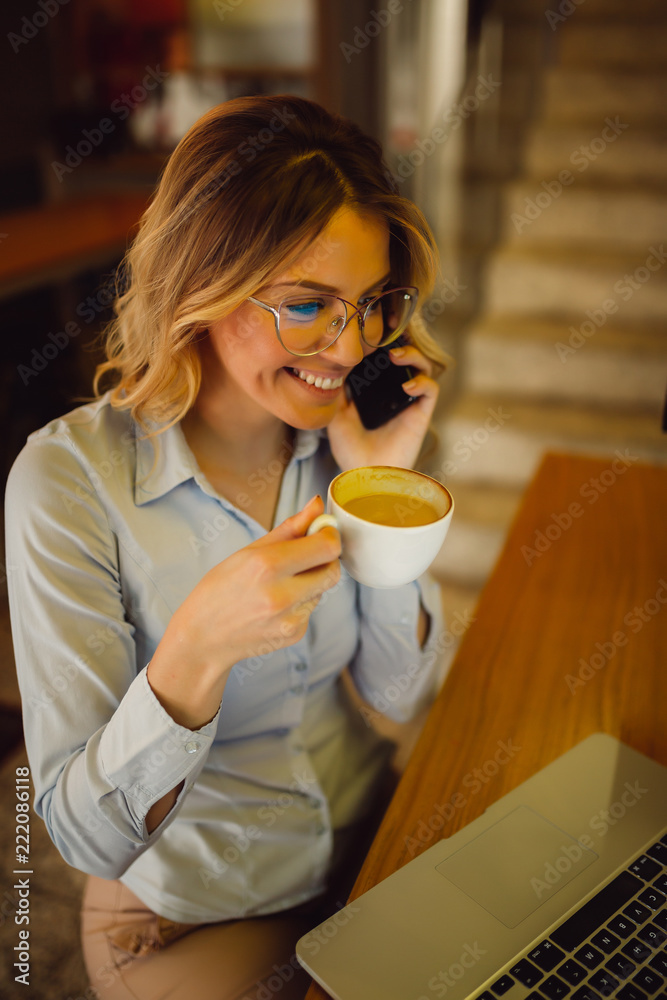 Cheerful beautiful woman with glasses talking on mobile phone drinking coffee with smile while sitting at cafeteria Cheerful beautiful woman with glasses talking on mobile phone drinking coffee with smile while sitting at cafeteria