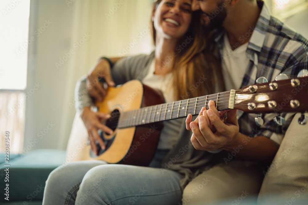 Close shot of young bearded man who teaches his girlfriend to play guitar.