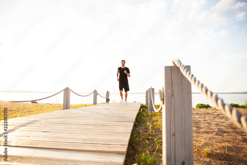 Full length shot of healthy young man running on the promenade. Male runner sprinting outdoors