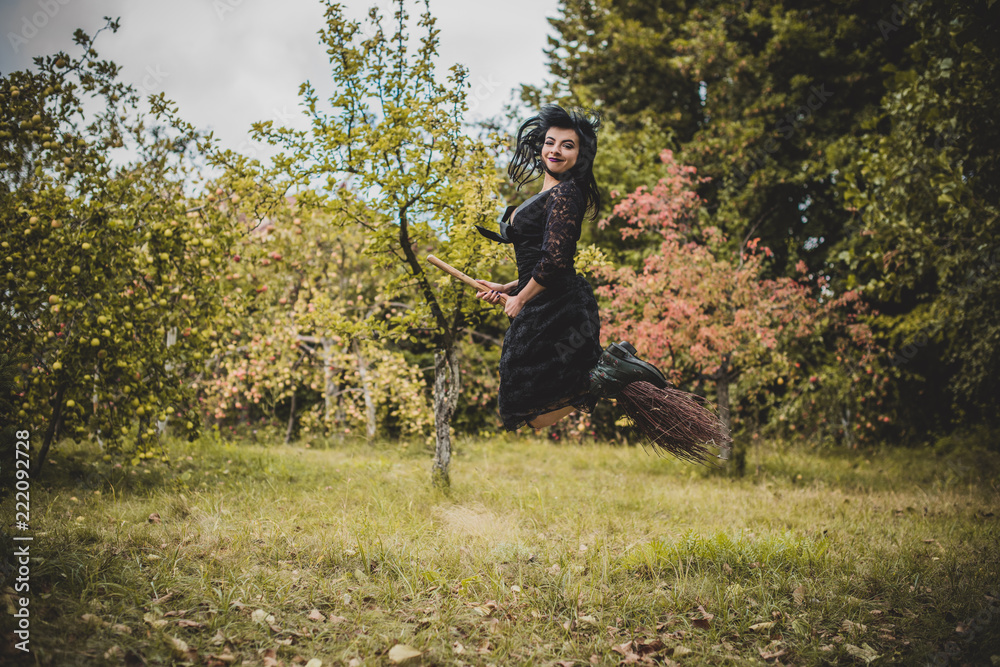 Young beautiful and mysterious Witch woman Flying on the Broom in woods. Levitation, a witch in a hat flies on a broom, free space. Halloween holiday, magic Young beautiful and mysterious Witch woman Flying on the Broom in woods. Levitation, a witch in a hat flies on a broom, free space. Halloween holiday, magic