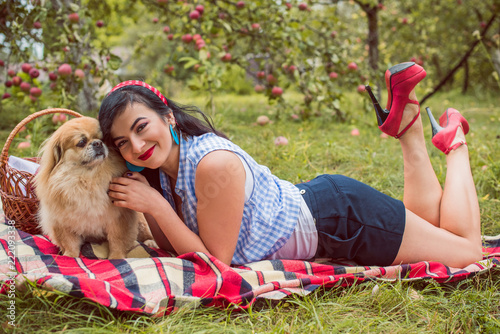 Young woman with her pekingese dog on picnic outside. Autumn time. Vintage retro pin up style and pretty day. Concept of human and pet  photo