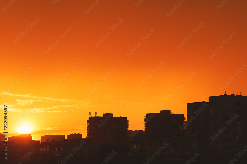 Bright orange sunset over the evening city. Bright lights of tall buildings of urban buildings. Great disk of the rising sun. Sun rays