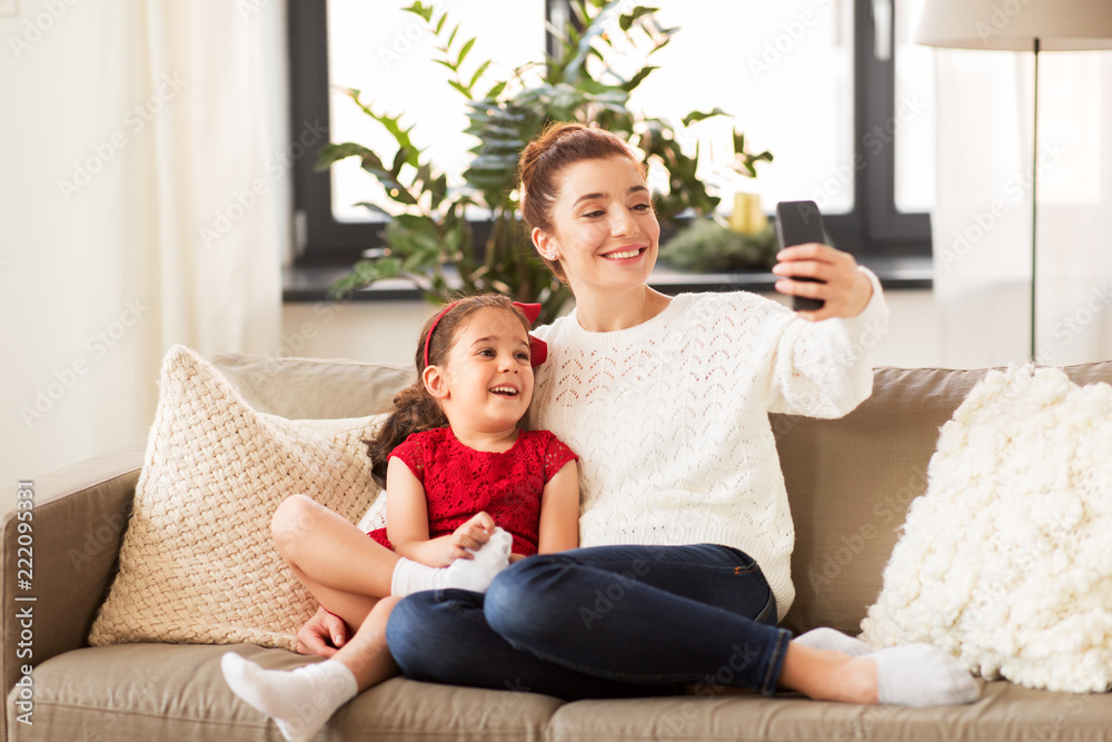 christmas, technology and family concept - happy mother and little daughter taking selfie by smartphone at home