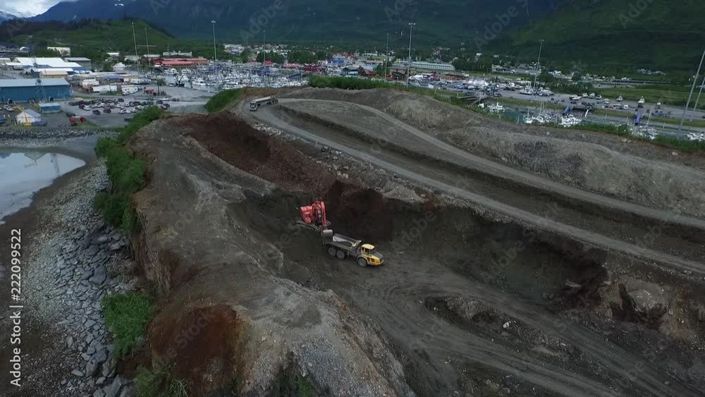 Excavator filling a off road dump truck, with job site materials on a waterfront project in