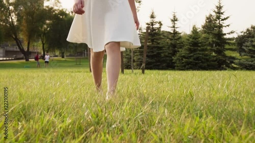 Beautiful little girl goes barefoot on grass in sunny summer park