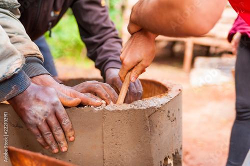 close up of black and white hands cooperating to build cement water well in africa village