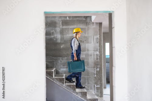 Woman worker with a tool box walking down the stairs on the construction site. © Halfpoint