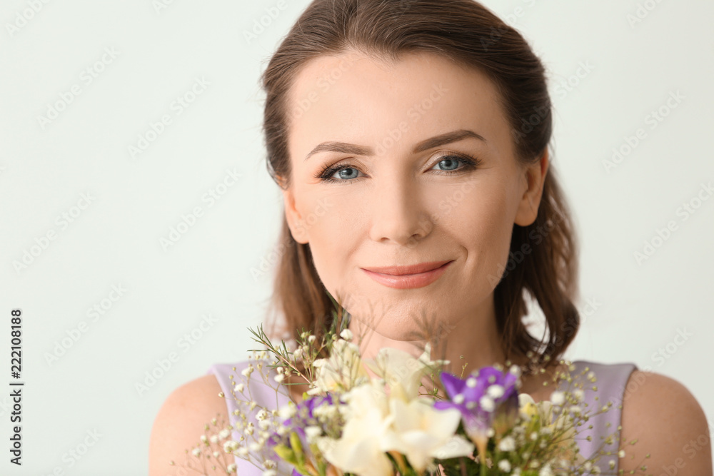 Beautiful woman with bouquet of flowers on light background