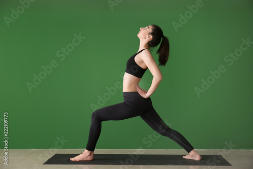 Young woman practicing yoga on near color wall