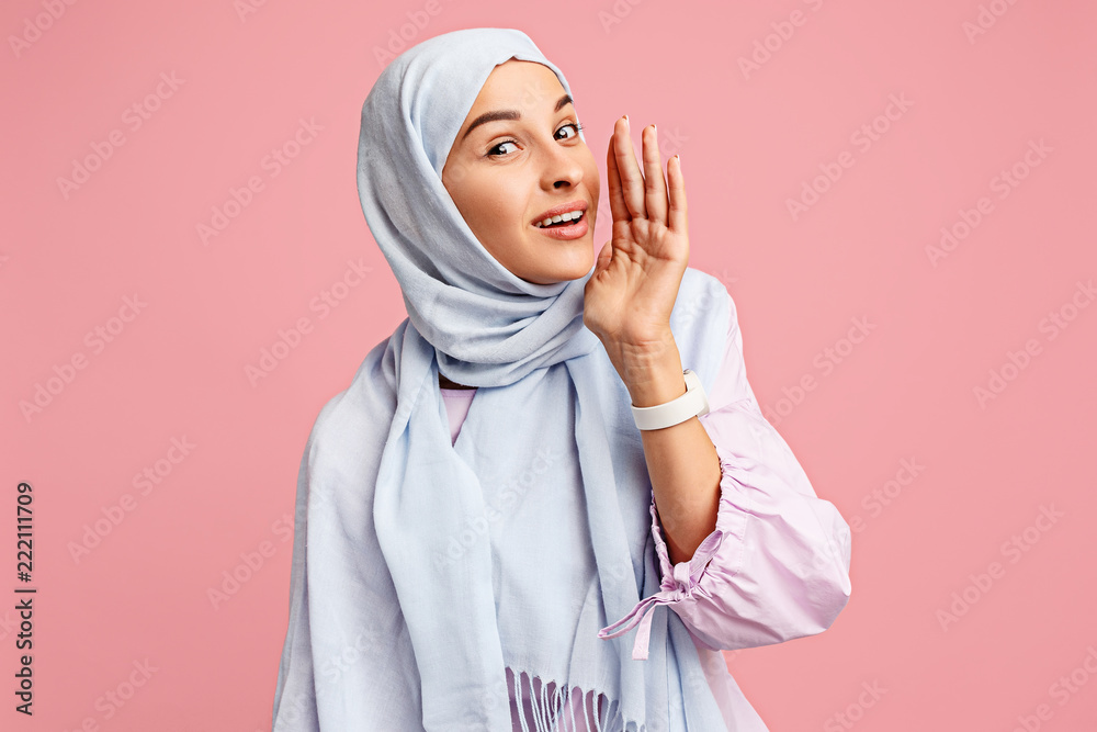 Secret, gossip concept. Happy arab woman in hijab. Portrait of smiling girl, posing at pink studio background. Young emotional woman. The human emotions, facial expression concept. Front view. Secret, gossip concept. Happy arab woman in hijab. Portrait of smiling girl, posing at pink studio background. Young emotional woman. The human emotions, facial expression concept. Front view.