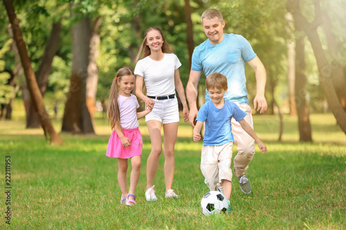 Happy family playing football in park on summer day