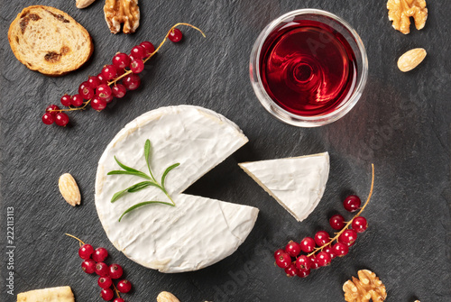 An overhead photo of Camembert cheese with a glass of red wine, fruits and nuts, shot from above on a black background