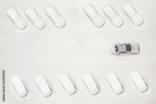 One car between of many snowy cars on the parkplace at the winter snowfall. Top or aerial view photo