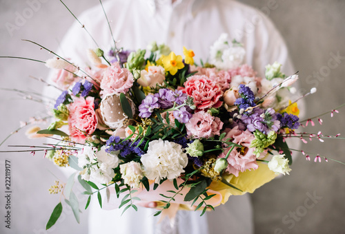 Fototapeta Naklejka Na Ścianę i Meble -  Very nice young man in a white shirt holding blossoming flower bouquet of  carnations, roses, eustoma,narcissus in vibrant colors on the grey wall background
