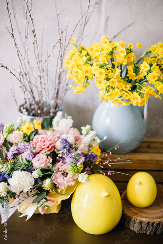 Fototapeta Naklejka Na Ścianę i Meble -  Two beautiful decorative ceramic yellow chickens, fresh blossoming flower basket, blue vase with yellow Narcissus and fluffy willow on the rustic wooden table 