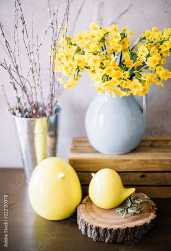 Fototapeta Naklejka Na Ścianę i Meble -  Two beautiful decorative ceramic yellow chickens, fresh blossoming flower basket, blue vase with yellow Narcissus and fluffy willow on the rustic wooden table 