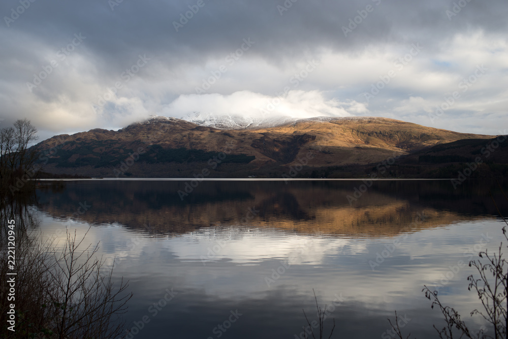 Ben Lomond reflected in Loch Lomond in Scotland with cloud cover at the summit.