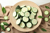 Wooden plate with sliced zucchini on table, top view