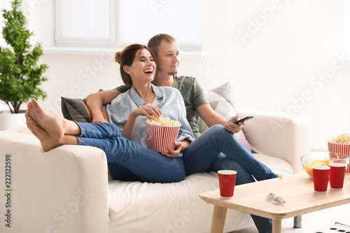 Couple eating popcorn while watching TV at home