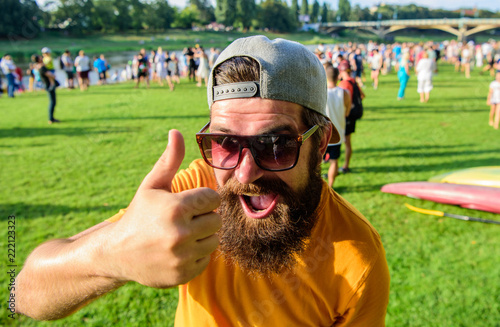 Top list summer festival must visit. Highly recommend top list. Hipster visiting event picnic fest or festival. Man bearded in front of crowd riverside background. Man cheerful face shows thumb up