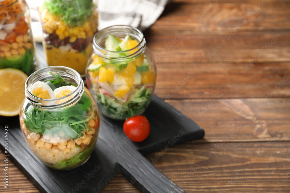 Delicious vegetable salads with egg in mason jars on wooden board