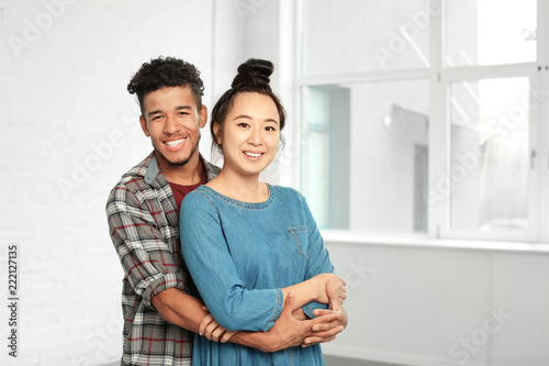 Happy interracial couple in empty room. Moving into new house © Pixel-Shot