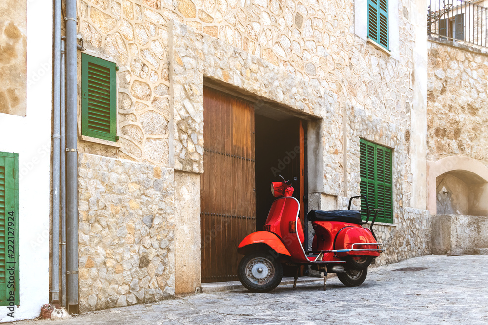 vintage red motor scooter parked on cobbled street in hostoric spanish village
