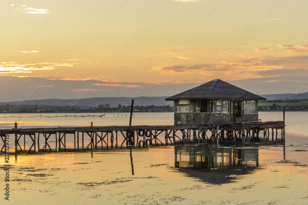 wooden Fishing hut in a lake with pier and fishing net at sunset.