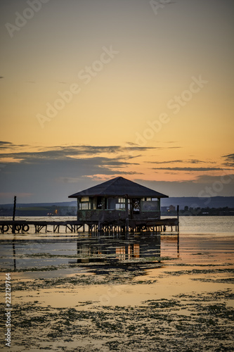 wooden Fishing hut in a lake with pier and fishing net at sunset.
