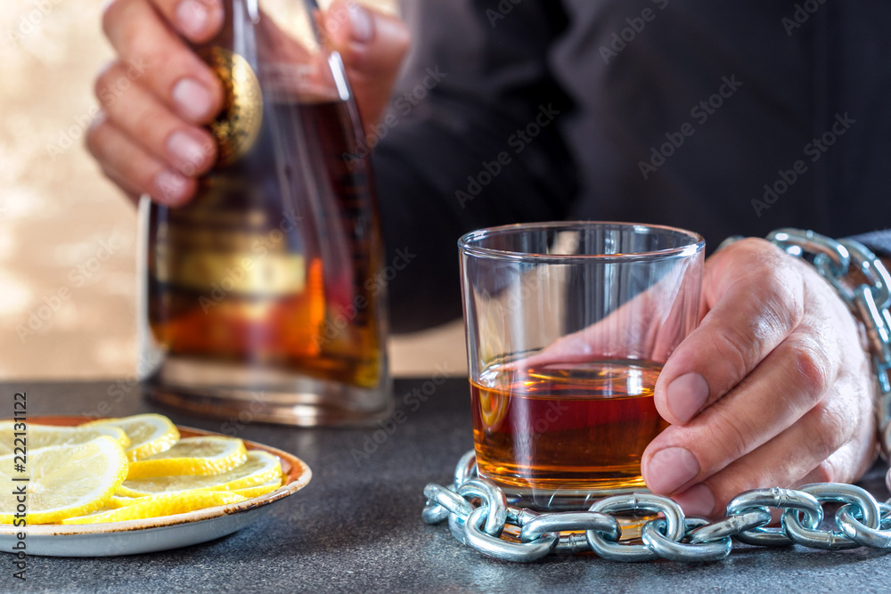 Hand of male chained to glass of alcohol drink.Alcohol dependence.Problem alcoholism in society. Hand of male chained to glass of alcohol drink.Alcohol dependence.Problem alcoholism in society.