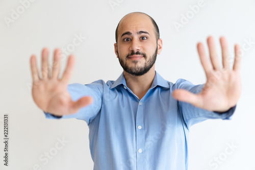 Friendly concerned office worker gesturing stop. Bald bearded Caucasian man in formal shirt showing both palms in handstop sign. Gesturing and warning concept photo