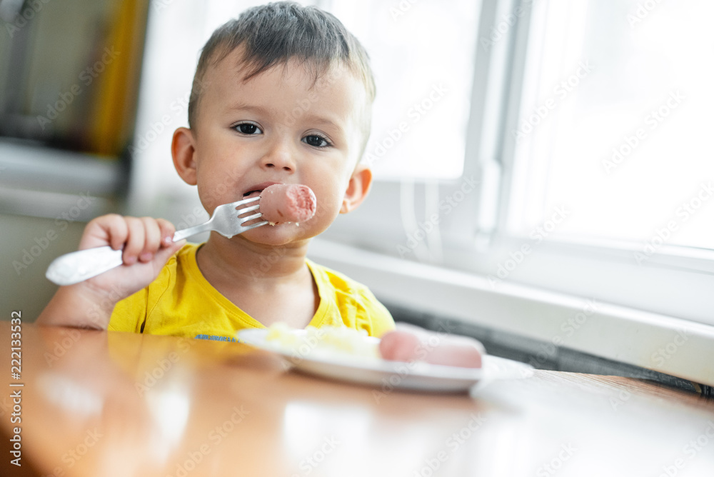 child in the kitchen eating sausage and mashed potatoes child in the kitchen eating sausage and mashed potatoes