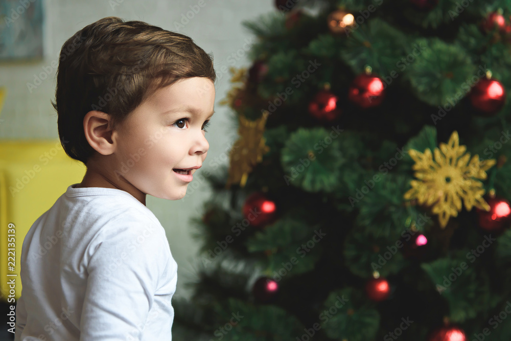 happy boy standing near christmas tree at home