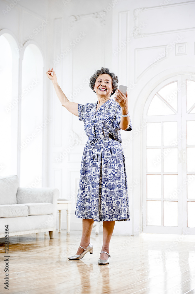 Asian grandmother with headphones listening to music dancing indoors