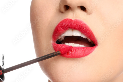 Beautiful young woman applying bright red lipstick on white background, closeup