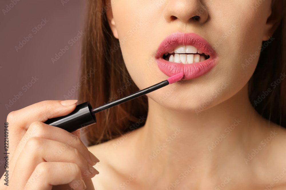 Fototapeta premium Beautiful young woman applying pink lipstick on color background, closeup